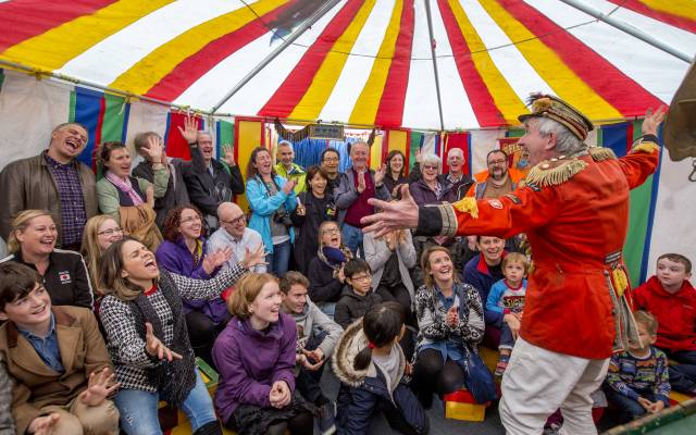 Puppet Festival A man in circus costume performing to an audience in a colourful tent