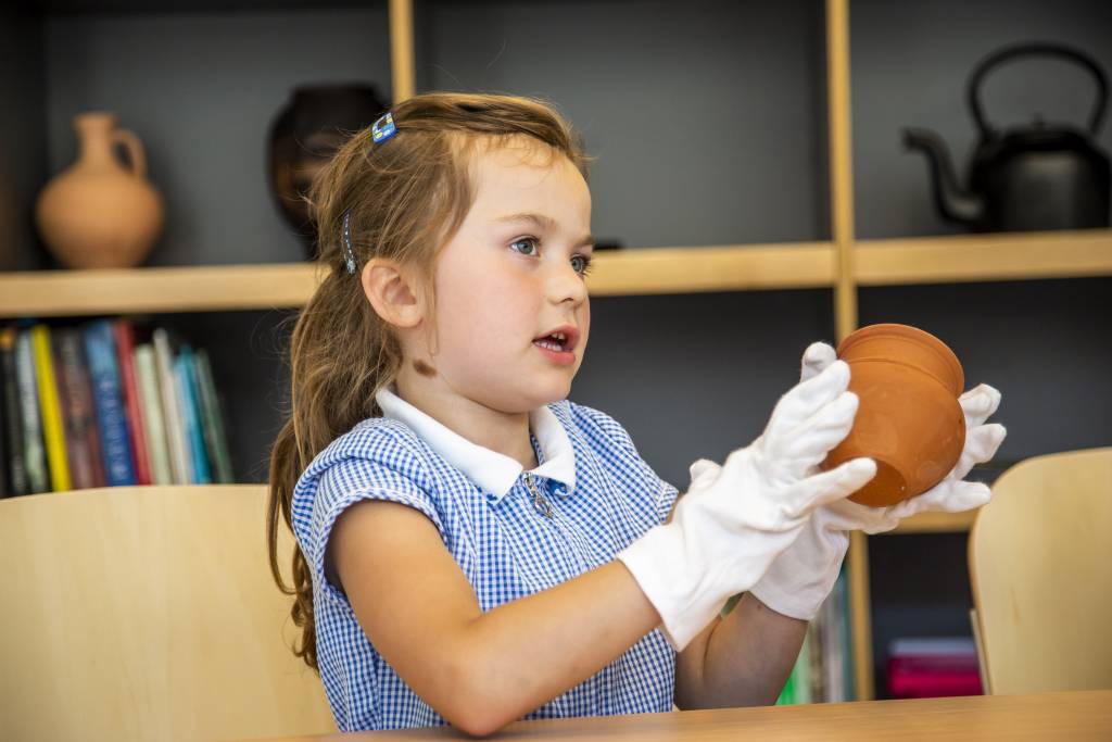 Skipton Town Hall_19 Young girl wearing a blue gingham school uniform dress is wearing white gloves and handling a clay pot.